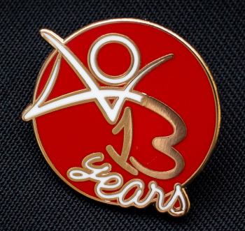 AO3 pin design: a red circle decorated with the AO3 logo and the words '13 years' in cursive font. The logo and the word 'years' are white and the number 13 is gold.