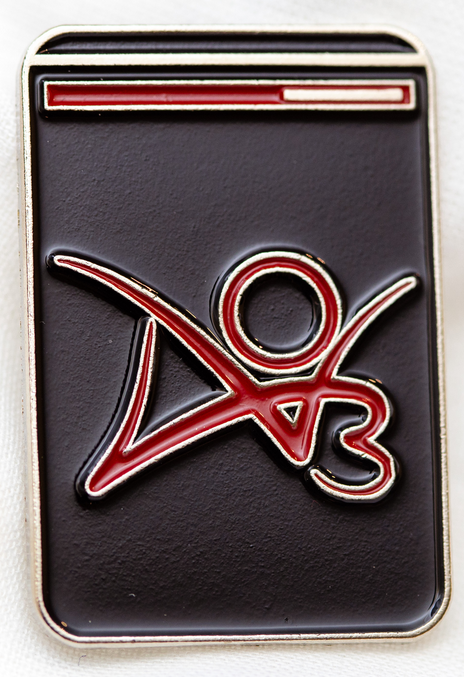 Pin dengan bidang memanjang hitam disertai logo AO3 berwarna merah di tengah serta bilah merah dan garis abu-abu pada bagian atas.